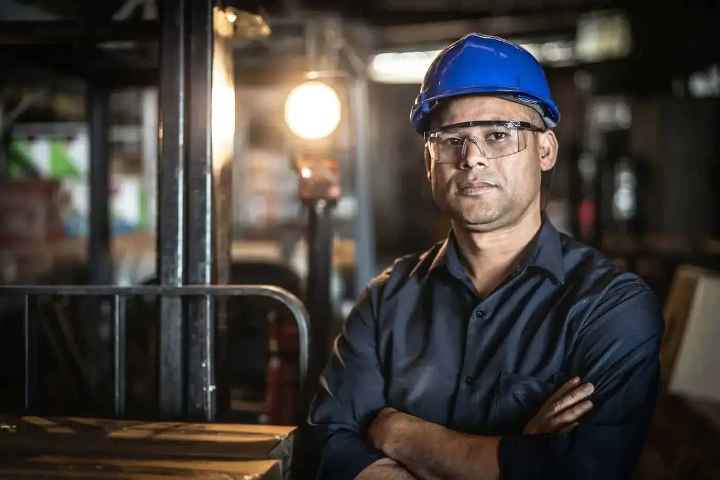 Industrial worker in a hard hat and safety glasses standing with arms crossed