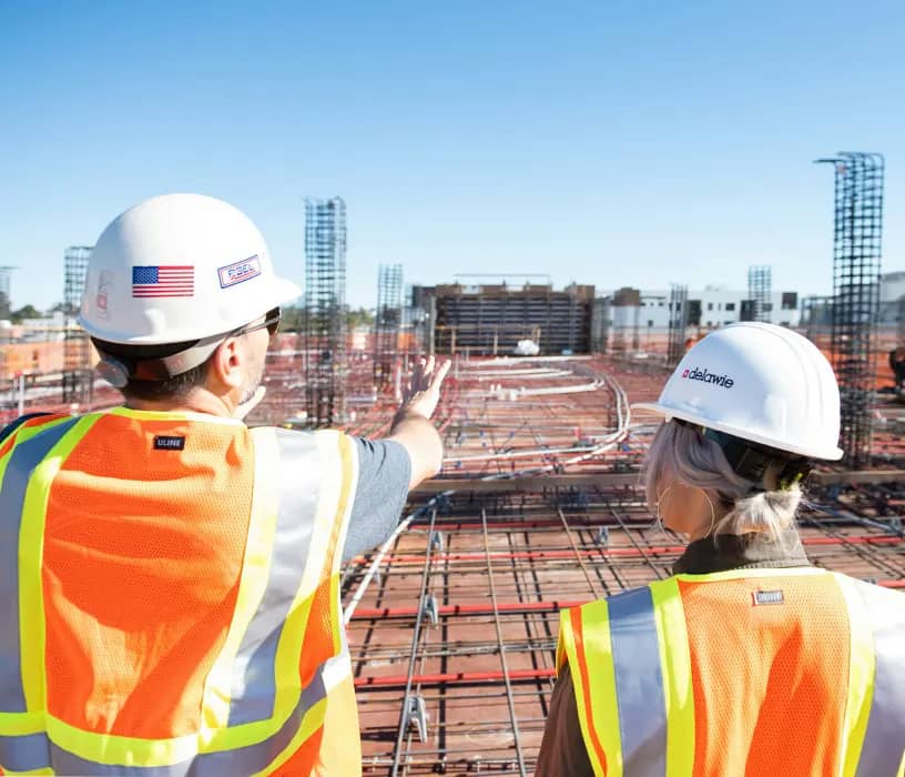 Two construction workers in safety gear overlooking a rebar foundation
