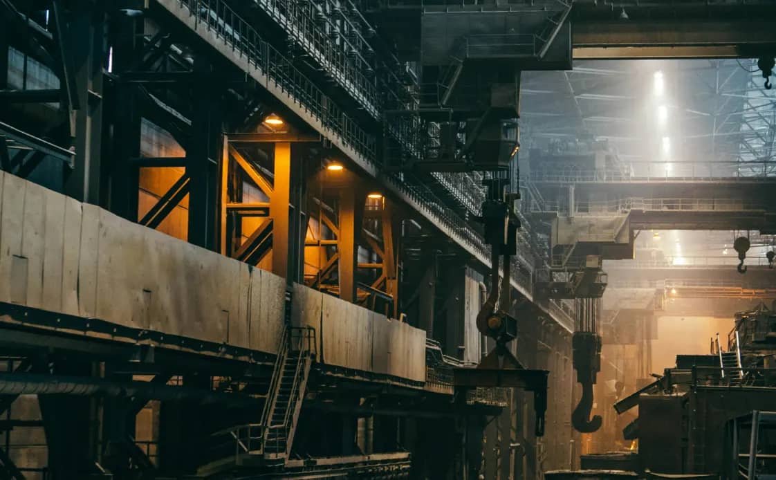 Dimly lit warehouse interior with overhead cranes and steel beams