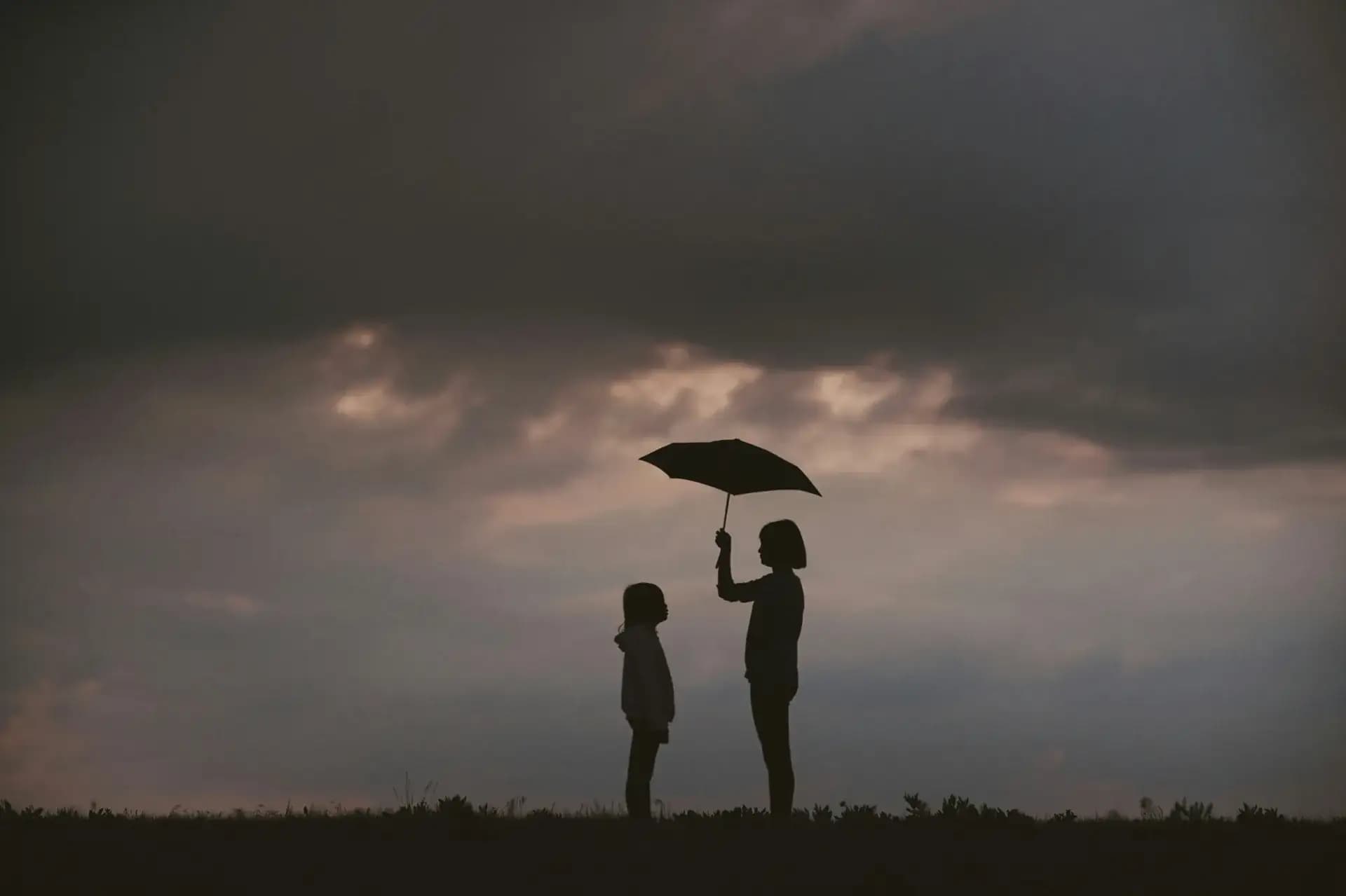 Silhouette of a woman and child under an umbrella at sunset